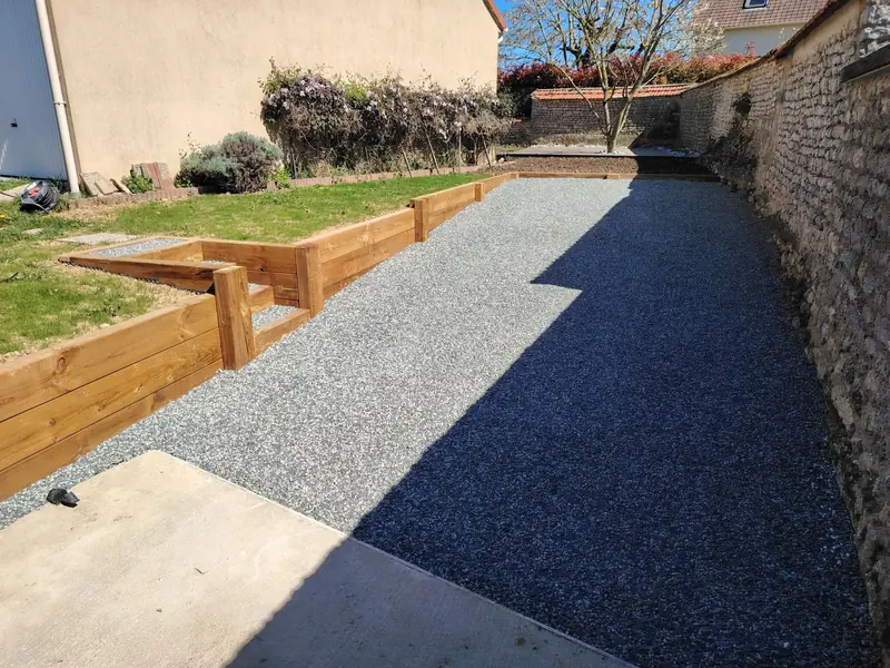 Deux places de stationnement en gravier stabilisé le long d’un vieux mur en pierre, murets et escalier en traverses côté jardin