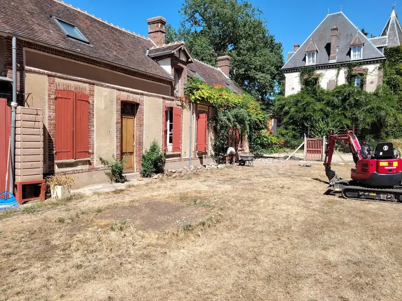 Mini-pelle sur le terrain en herbe sèche devant la maison, avant le début du décaissement