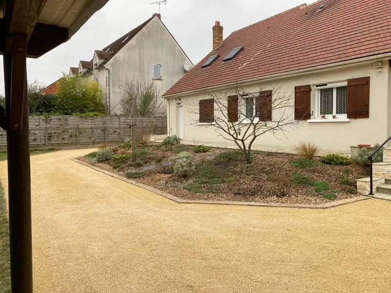 Allée carrossable en gravier stabilisé contournant un massif devant la maison