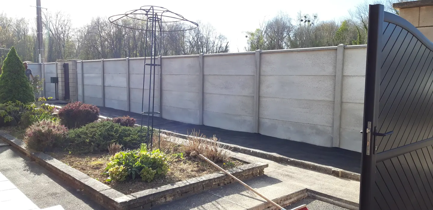 Clôture en plaques de béton gris clair derrière le massif fleuri