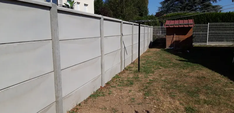 Clôture en plaques de béton le long d’un jardin, abri au fond