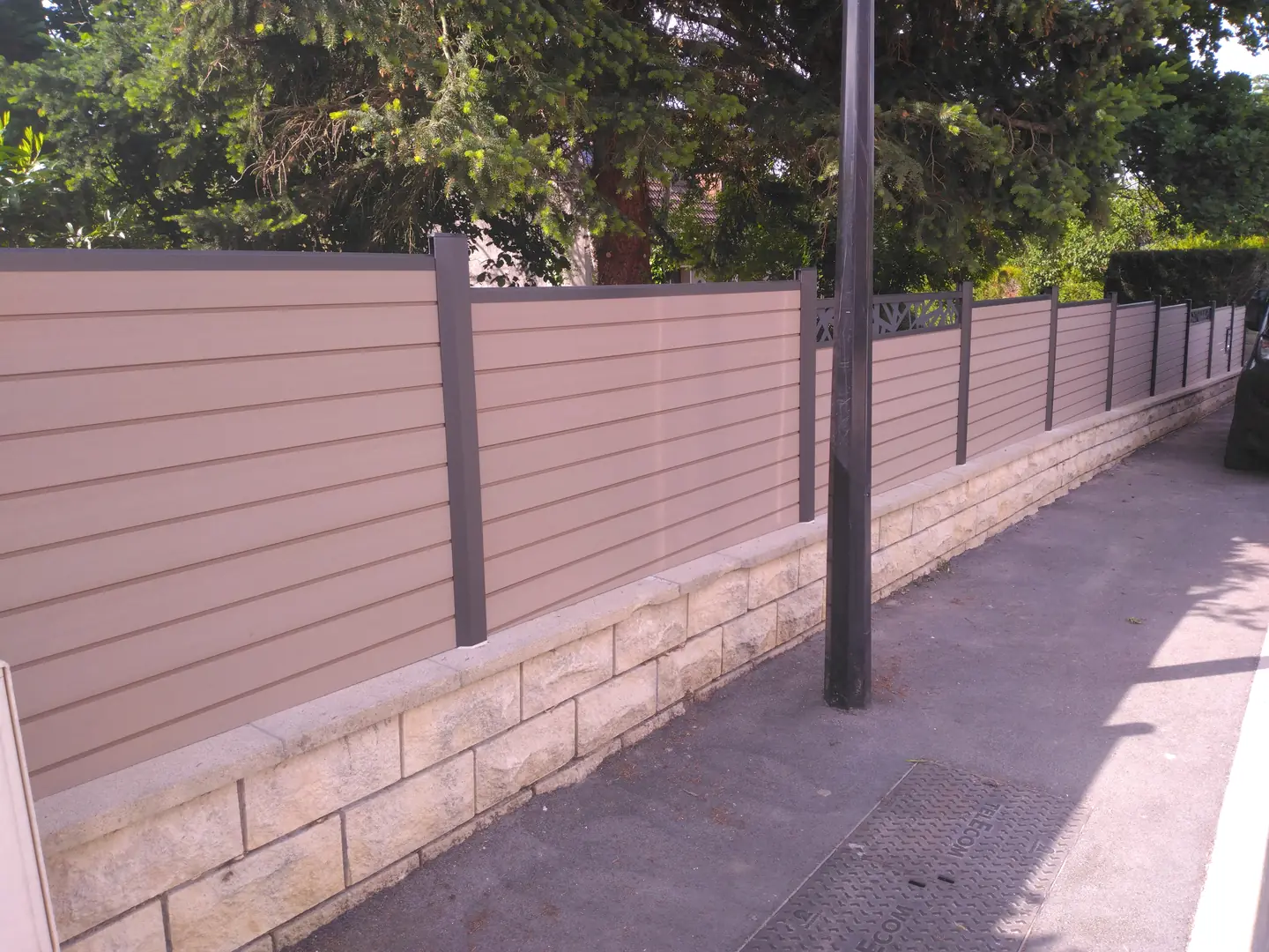 Clôture en lames composites sur muret parementé, le long du trottoir