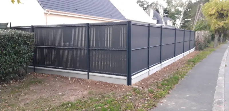 Clôture pleine grise sur muret, le long du trottoir
