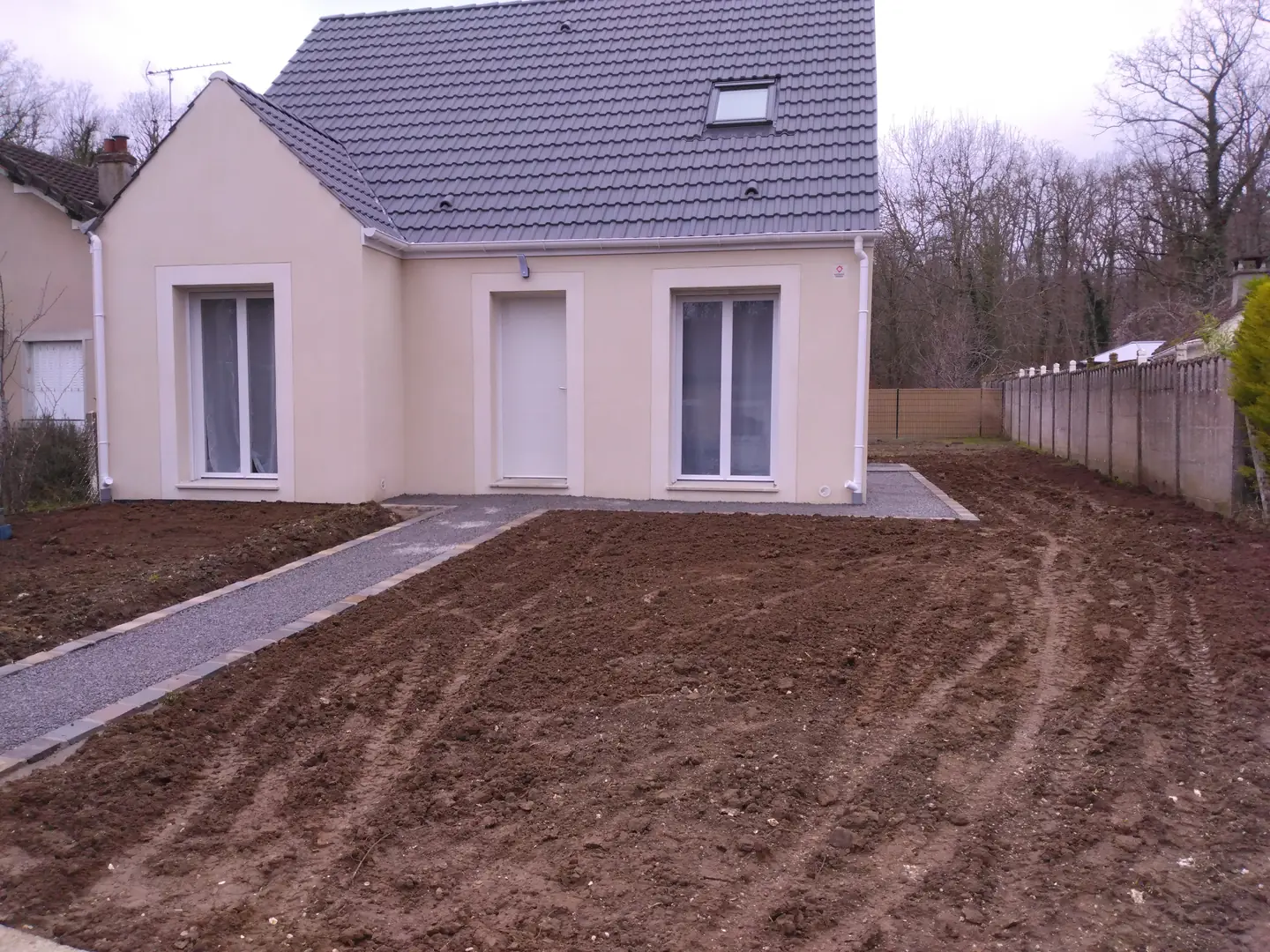 Terrain nu et allée posée devant une maison neuve, avant le gazon