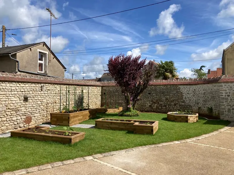 Bacs potagers en bois sur gazon neuf, entre les murs en pierre