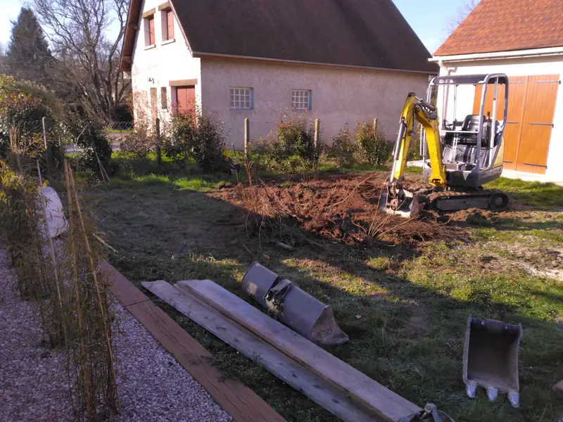 Mini-pelle extrayant une souche dans un jardin en terre, avant travaux