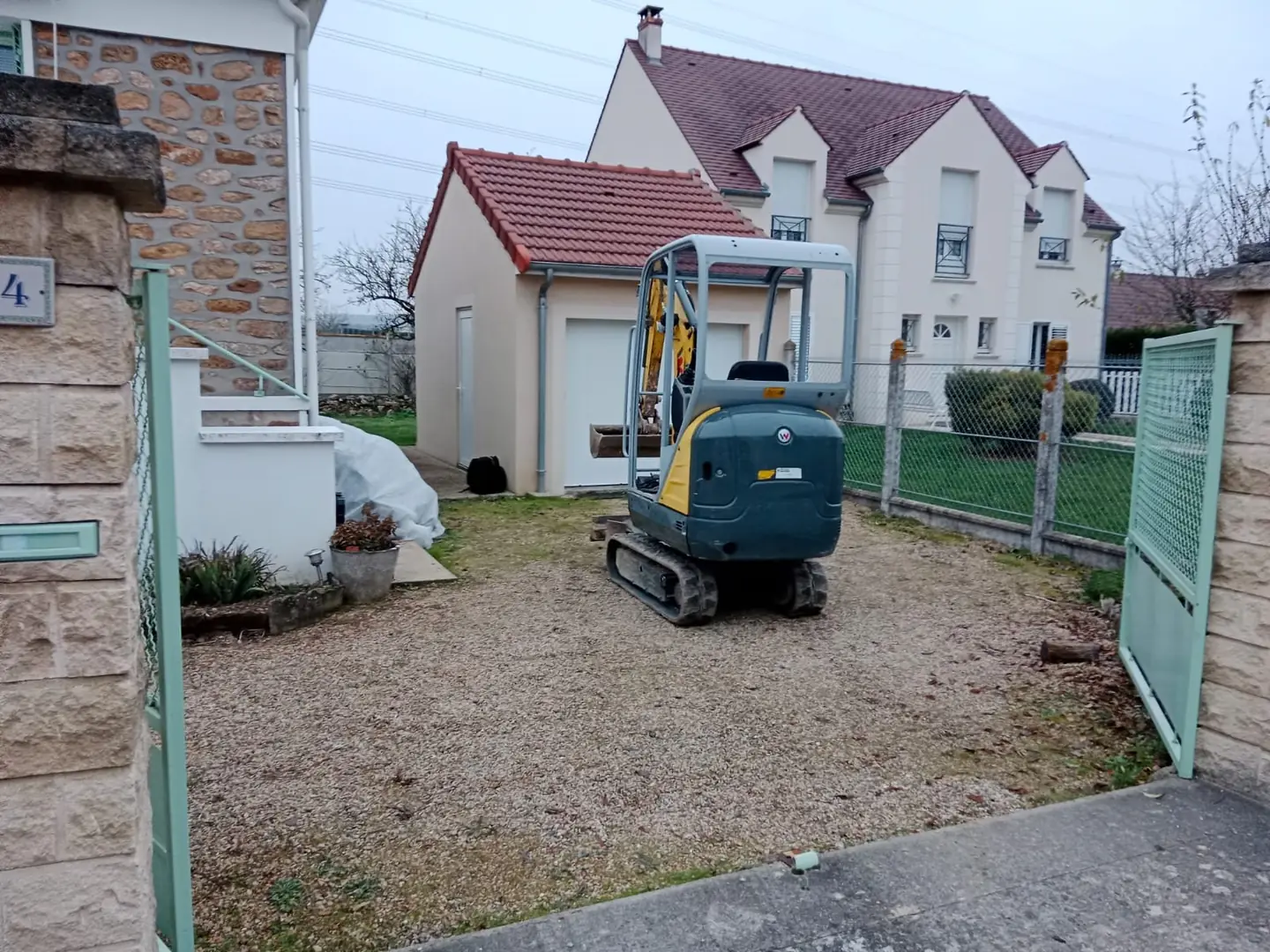 Mini-pelle dans une cour en terre devant la maison, avant travaux