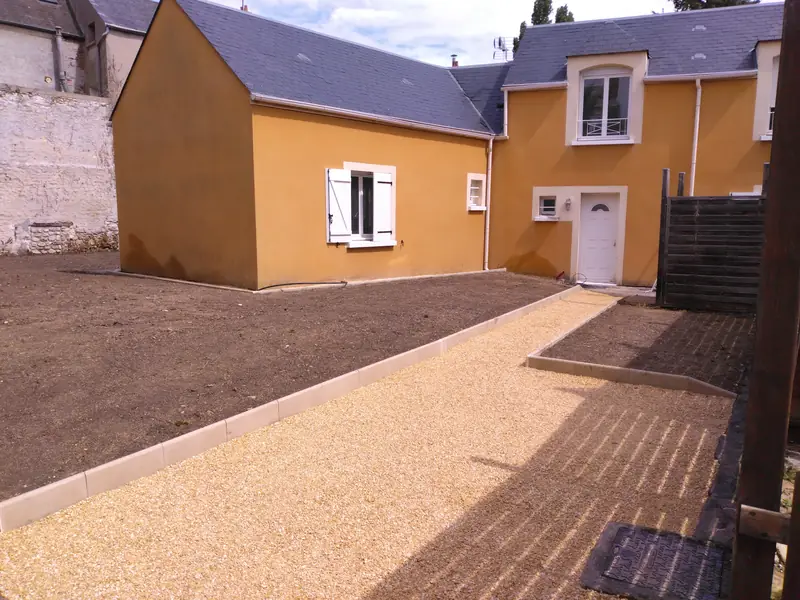 Allée en gravier stabilisé et bordure béton le long d’une maison orange